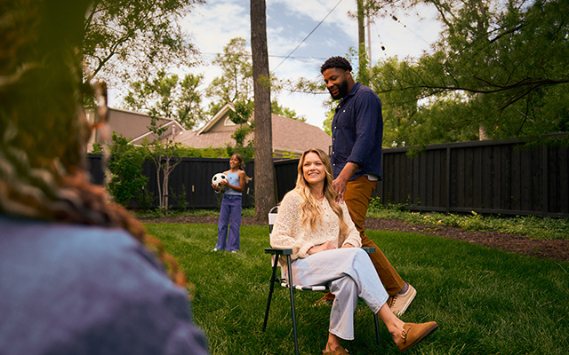 Wife sitting in lawn chair while her husband and child play soccer