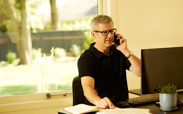 Older man talking on phone while looking at computer